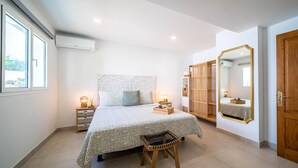 A bedroom with a bed, bedside tables, a chair, a wardrobe, a mirror, and a window. - CARTAMAR by Buenavilla | Refurbished villa with lots of outdoor space (Tías)