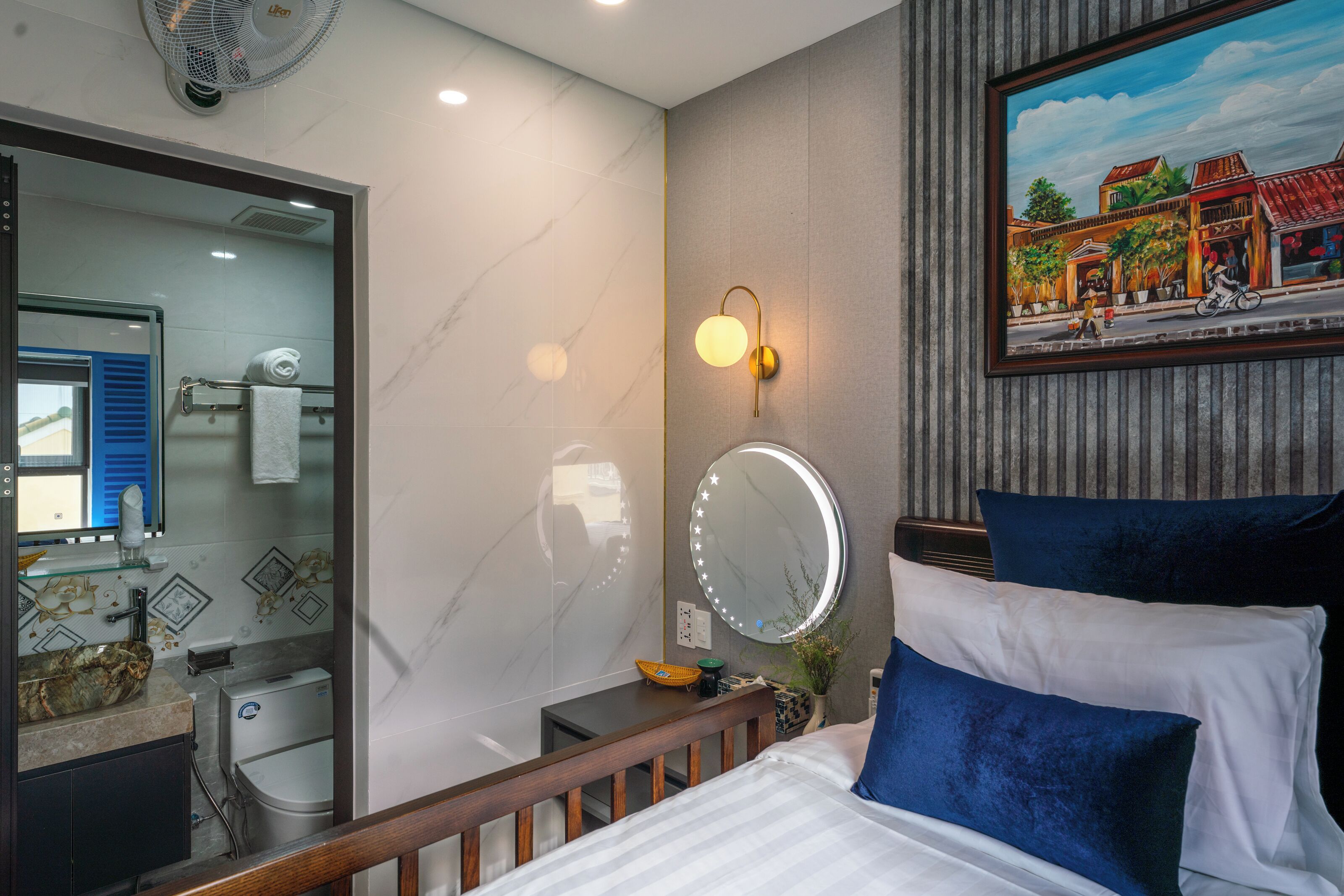 A hotel room with a bed, a bedside table, a mirror, a bathroom with a toilet, and a shower.