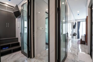 Quarto de hotel moderno com piso de mármore, televisão embutida e box de vidro.