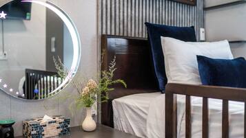 A neatly made bed with white and dark blue pillows, a bedside table with a vase of flowers, a mirror with a star light, and a small box of tissues.