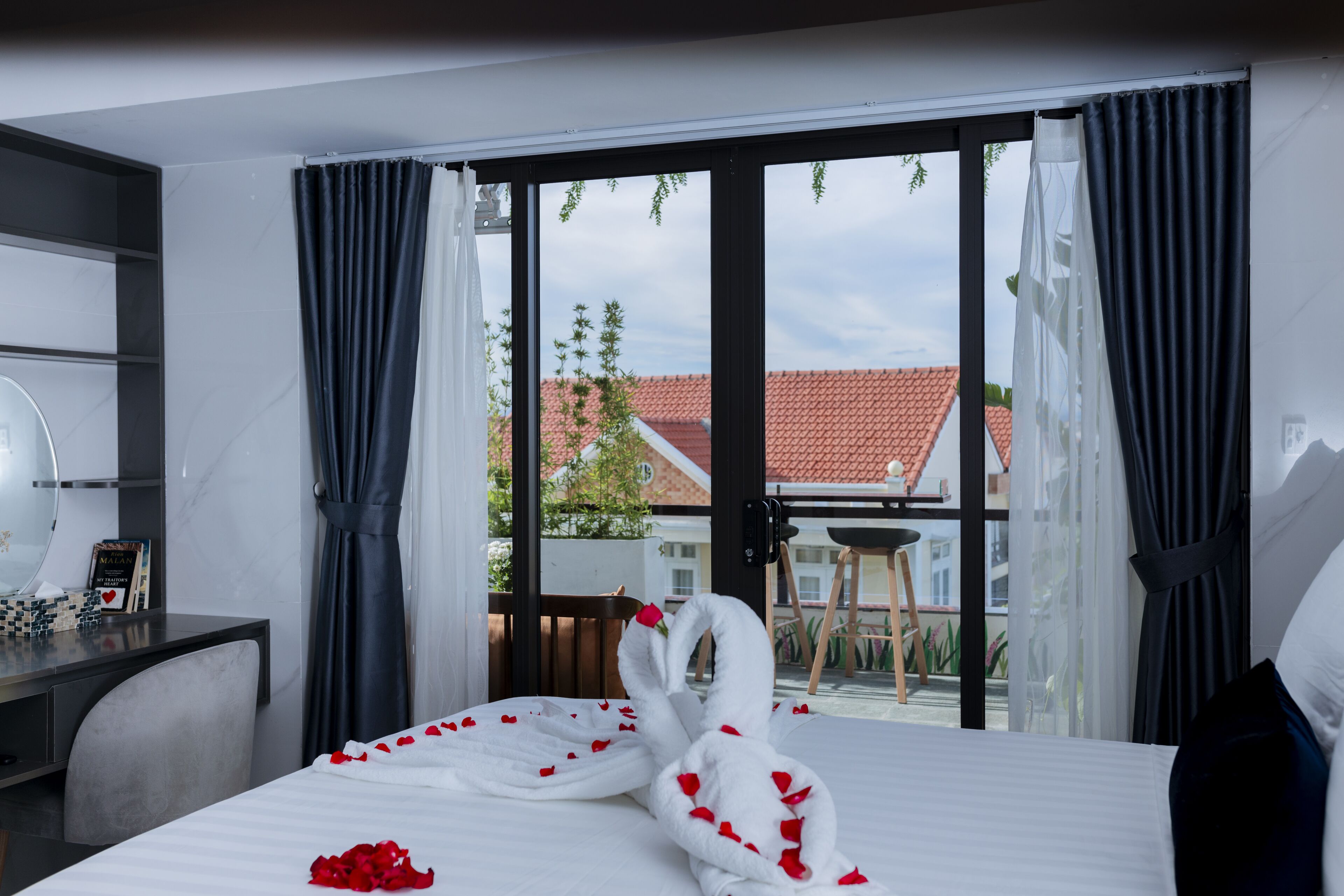 A hotel room with a bed, a desk, and a view of a building with a red roof.