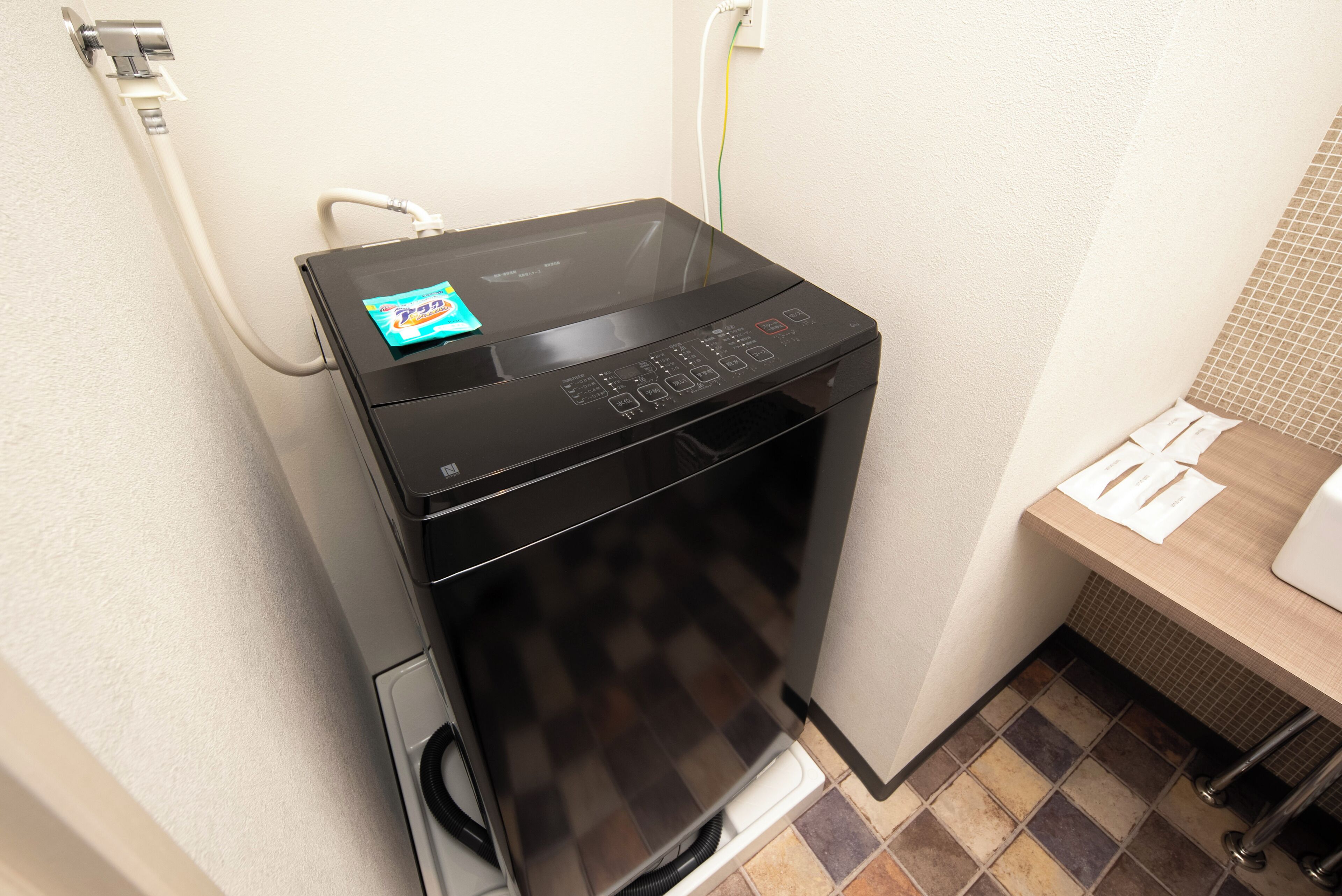 Un lave-linge compact et moderne dans une petite salle de bain, avec un sol carrelé, un lavabo et un porte-serviettes.