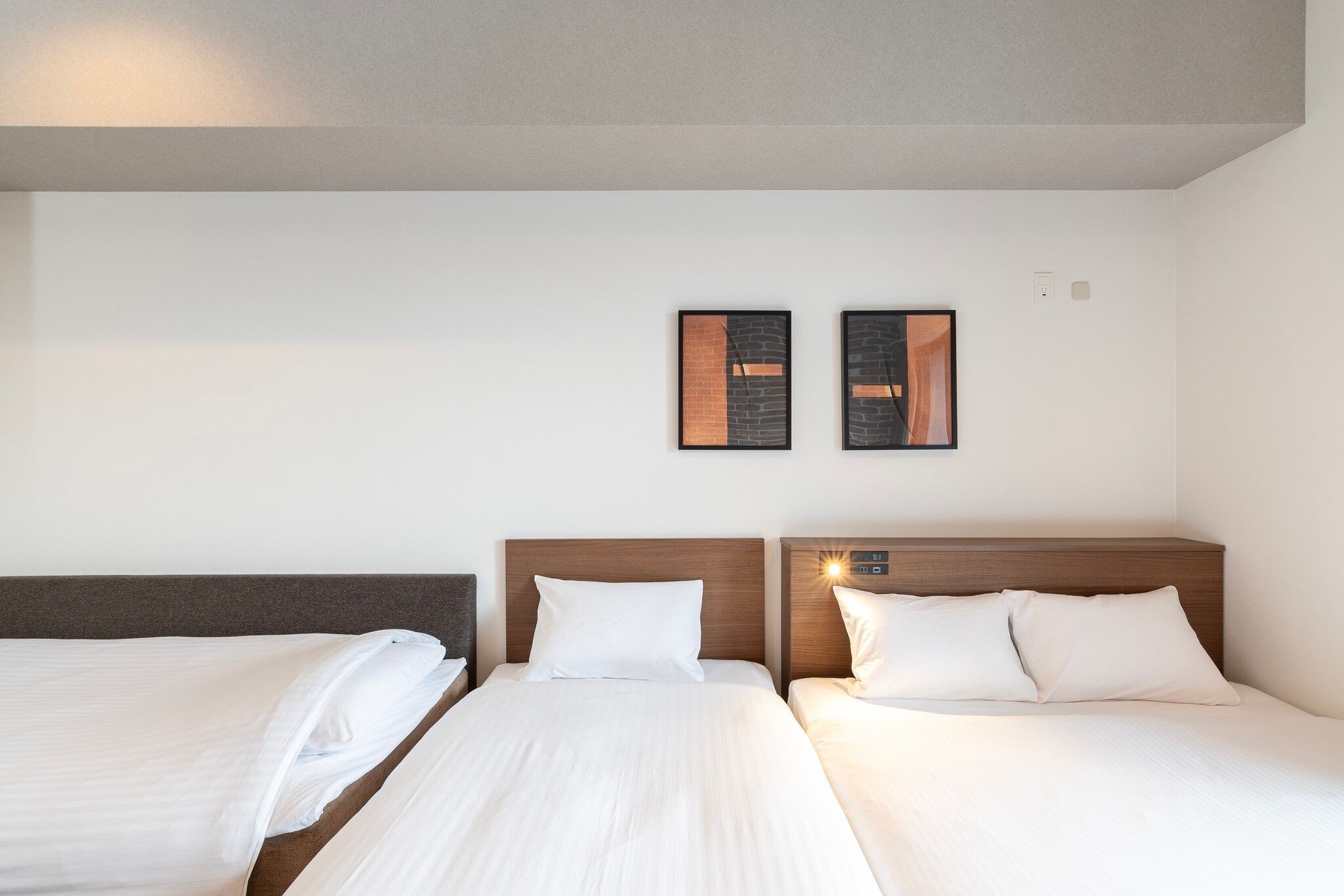 A hotel room with two beds, a wooden headboard, and two framed pictures on the wall.