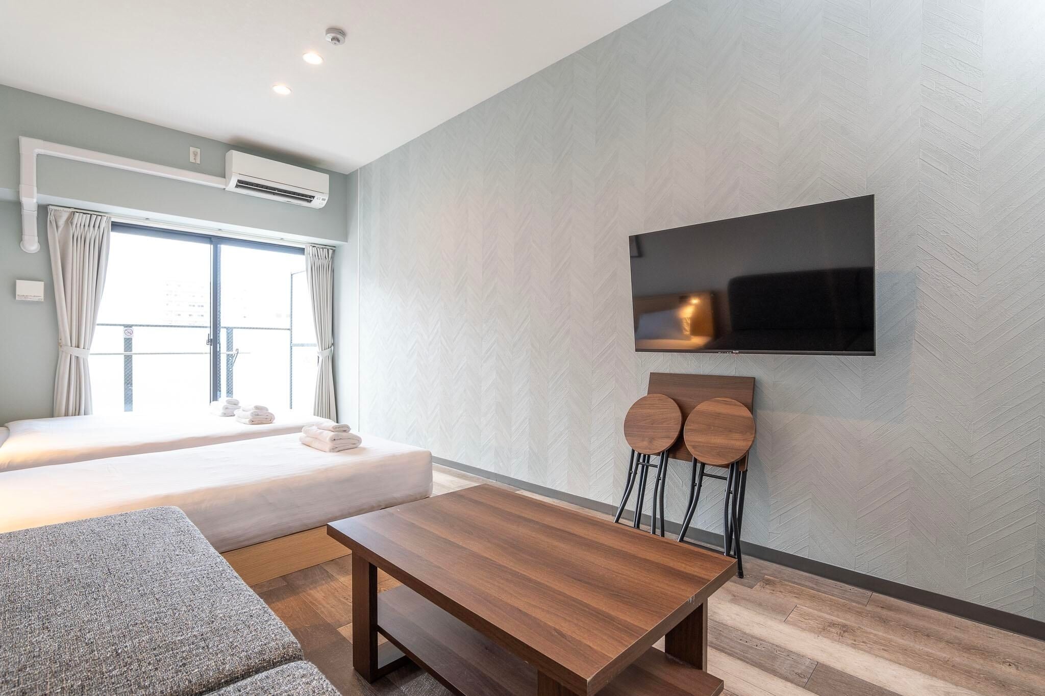 A modern hotel room with a bed, a TV mounted on the wall, a wooden table, and a sofa.