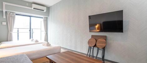 A modern hotel room with a bed, a TV mounted on the wall, a wooden table, and a sofa.