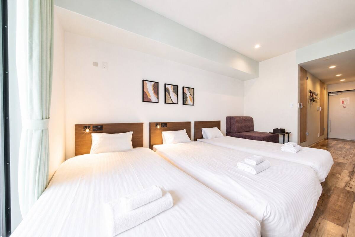 A hotel room with three beds, a wooden headboard, a small seating area, and artwork on the wall.