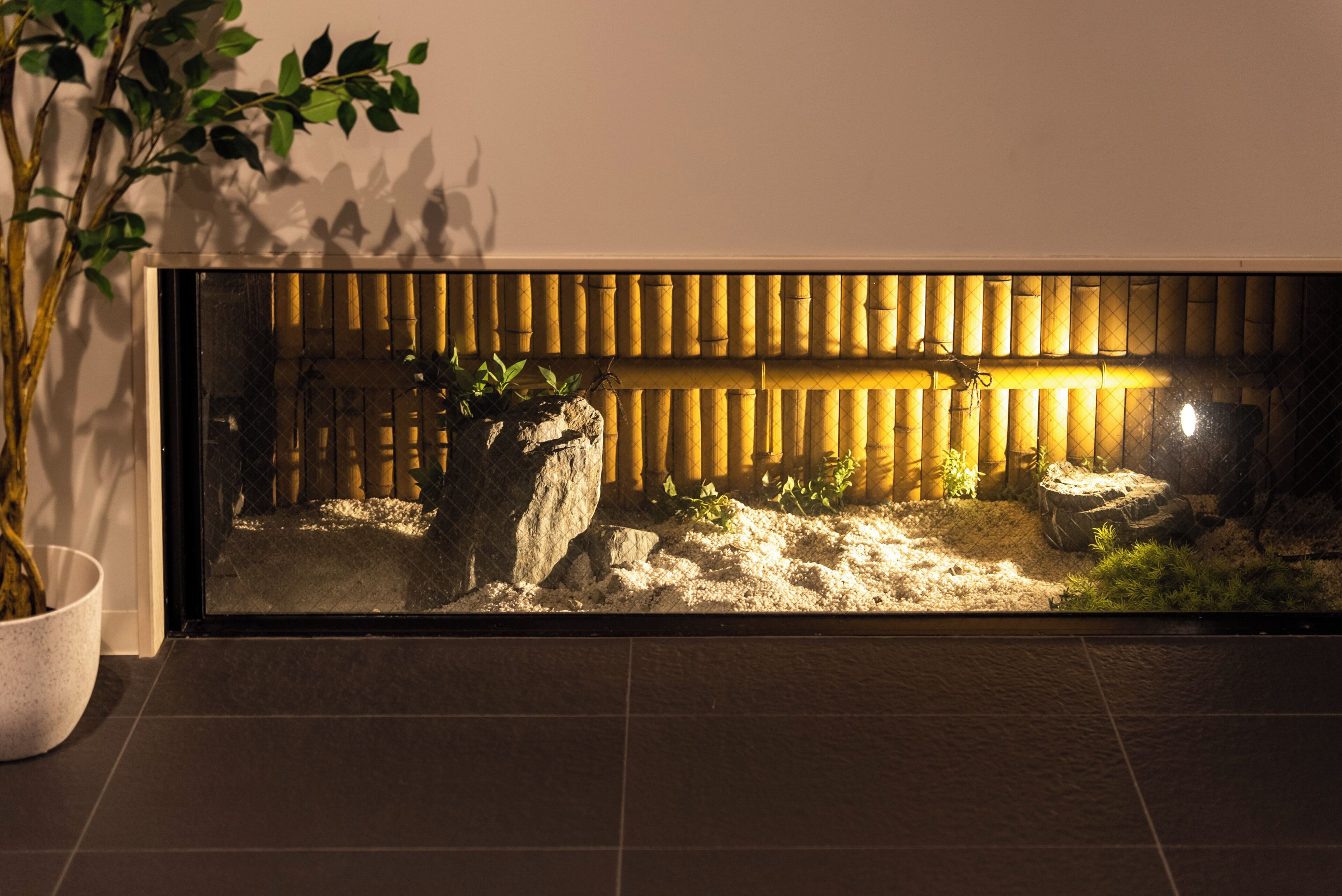 A rectangular aquarium with a bamboo backdrop, a rock formation, and aquatic plants.
