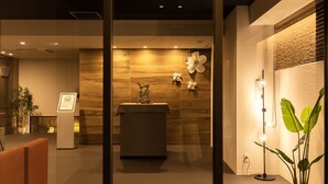 A reception area with a wooden wall, a reception desk, a potted plant, and a floor lamp.