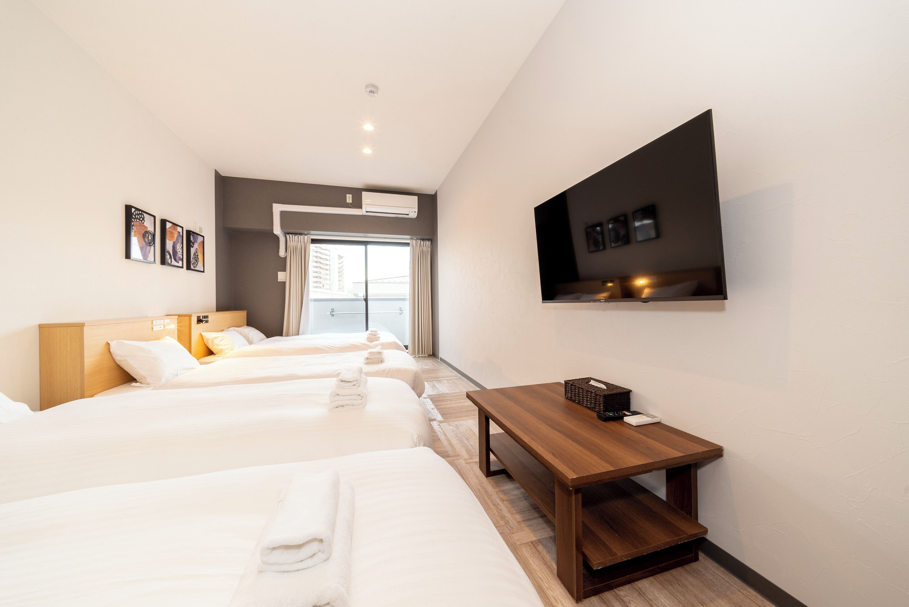 Habitación de hotel con tres camas, una mesa de madera, un televisor de pantalla plana y una ventana con cortinas.