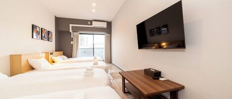 Habitación de hotel con tres camas, una mesa de madera, un televisor de pantalla plana y una ventana con cortinas.