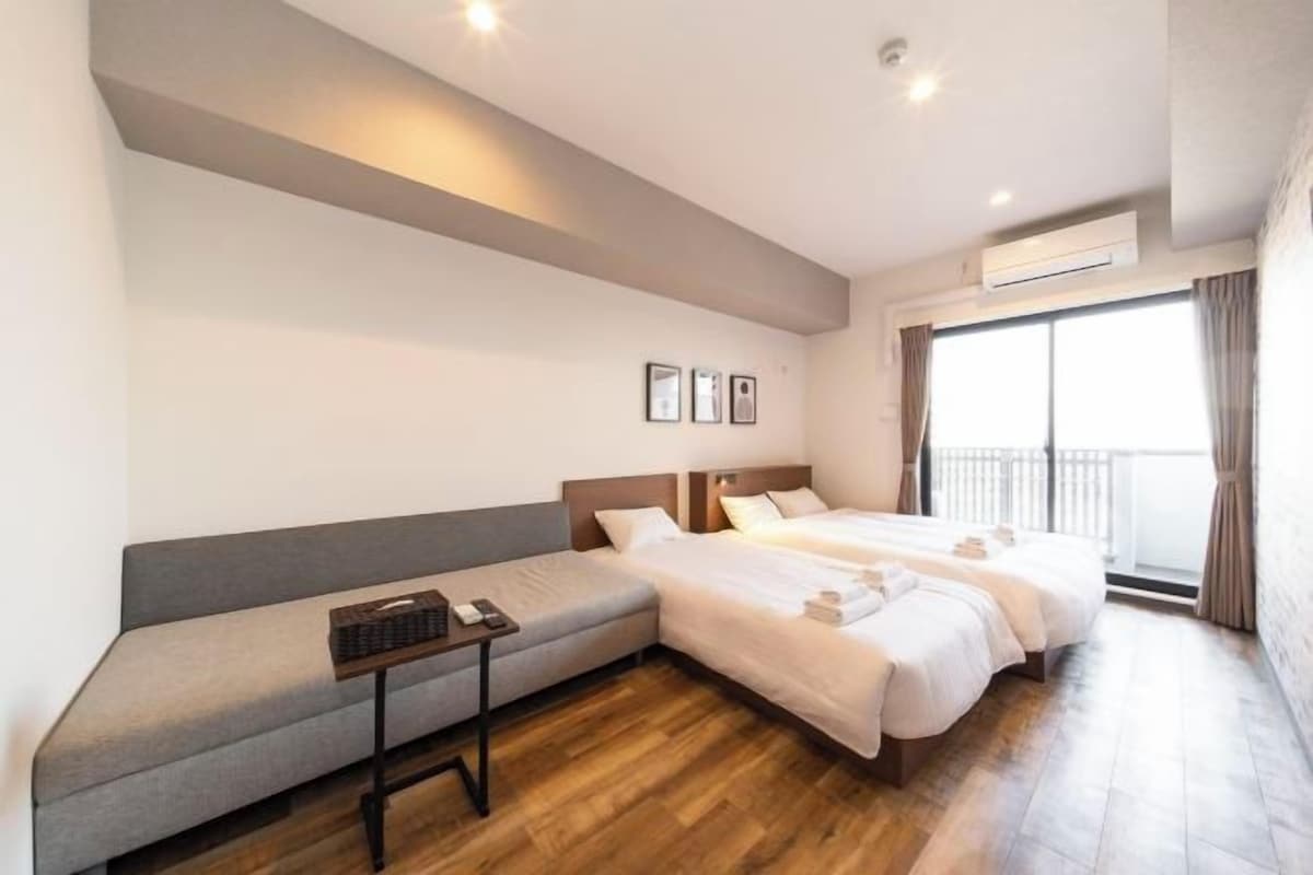 A hotel room with a sofa, two beds, a small table with a keyboard, and a window with curtains.