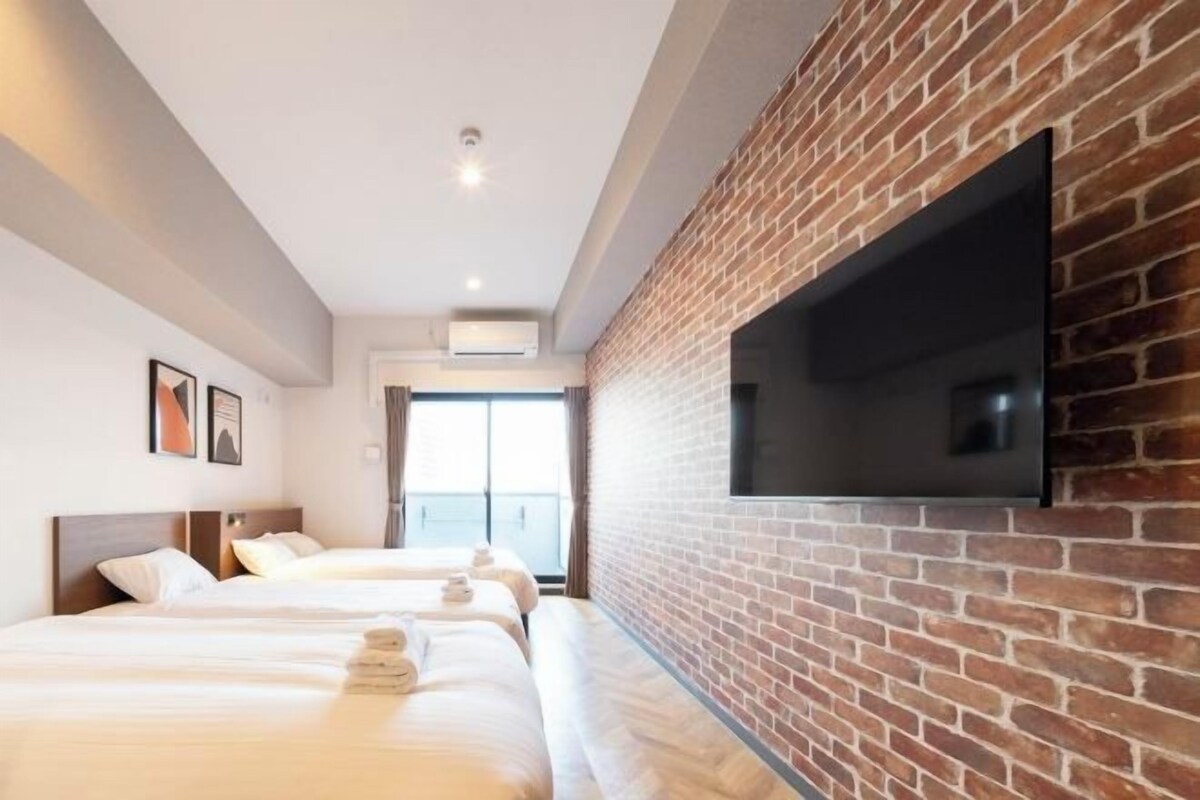 A hotel room with a brick wall, a flat-screen TV mounted on it, and a large window.