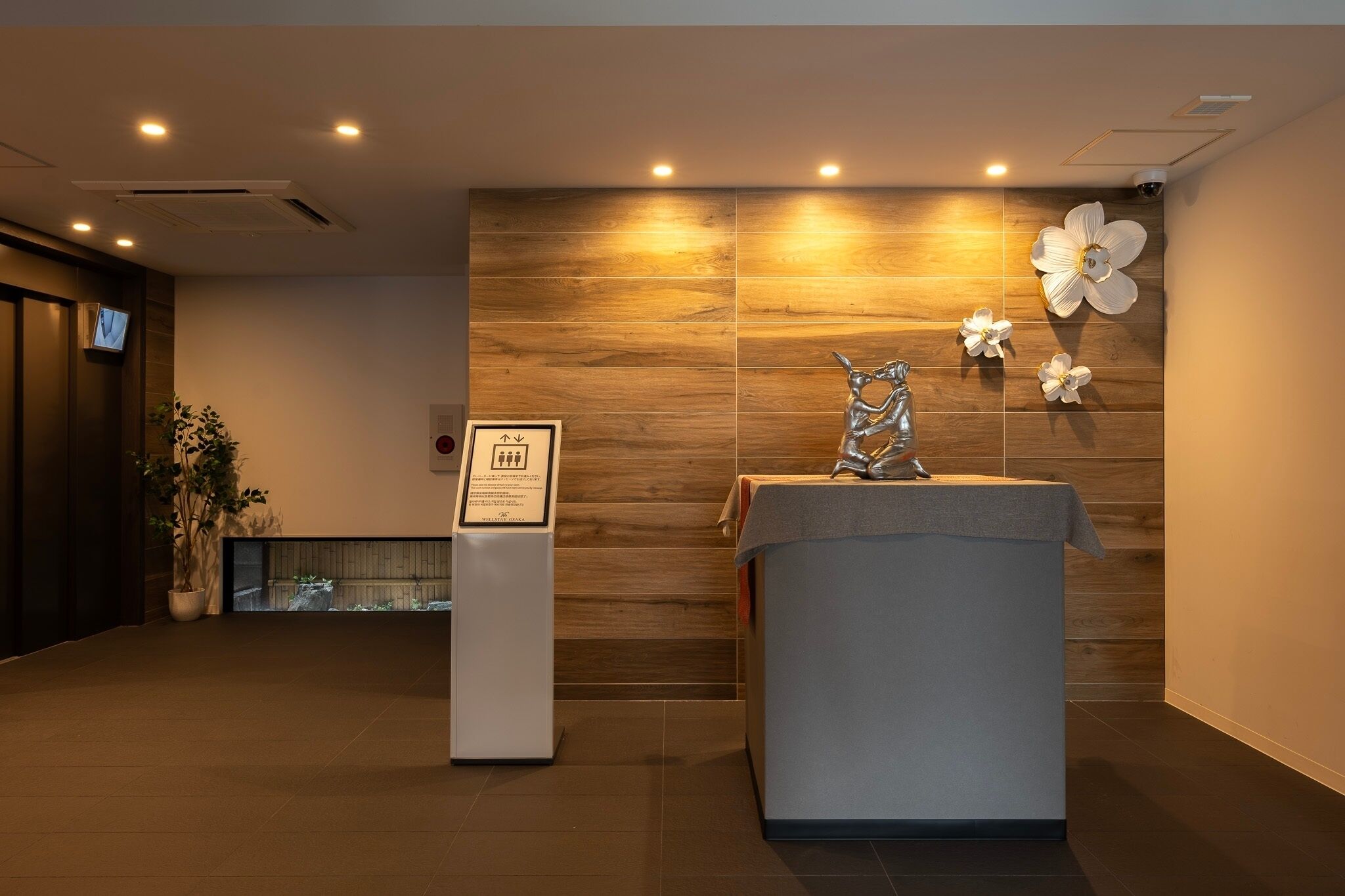 Un área de recepción con pared de madera, mostrador de recepción, un letrero y una escultura decorativa.