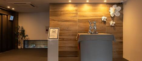 Un área de recepción con pared de madera, mostrador de recepción, un letrero y una escultura decorativa.