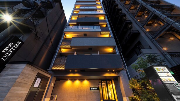 A modern hotel entrance with a 'Stay' sign, multiple balconies, and a vending machine.