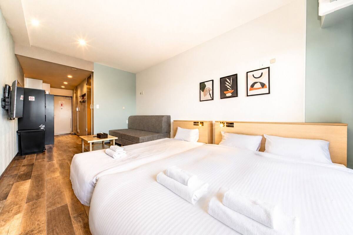 A hotel room with a large bed, a sofa, a small table, and a refrigerator.