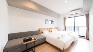 A modern hotel room with a sofa, two beds, a small table, and a balcony with curtains.