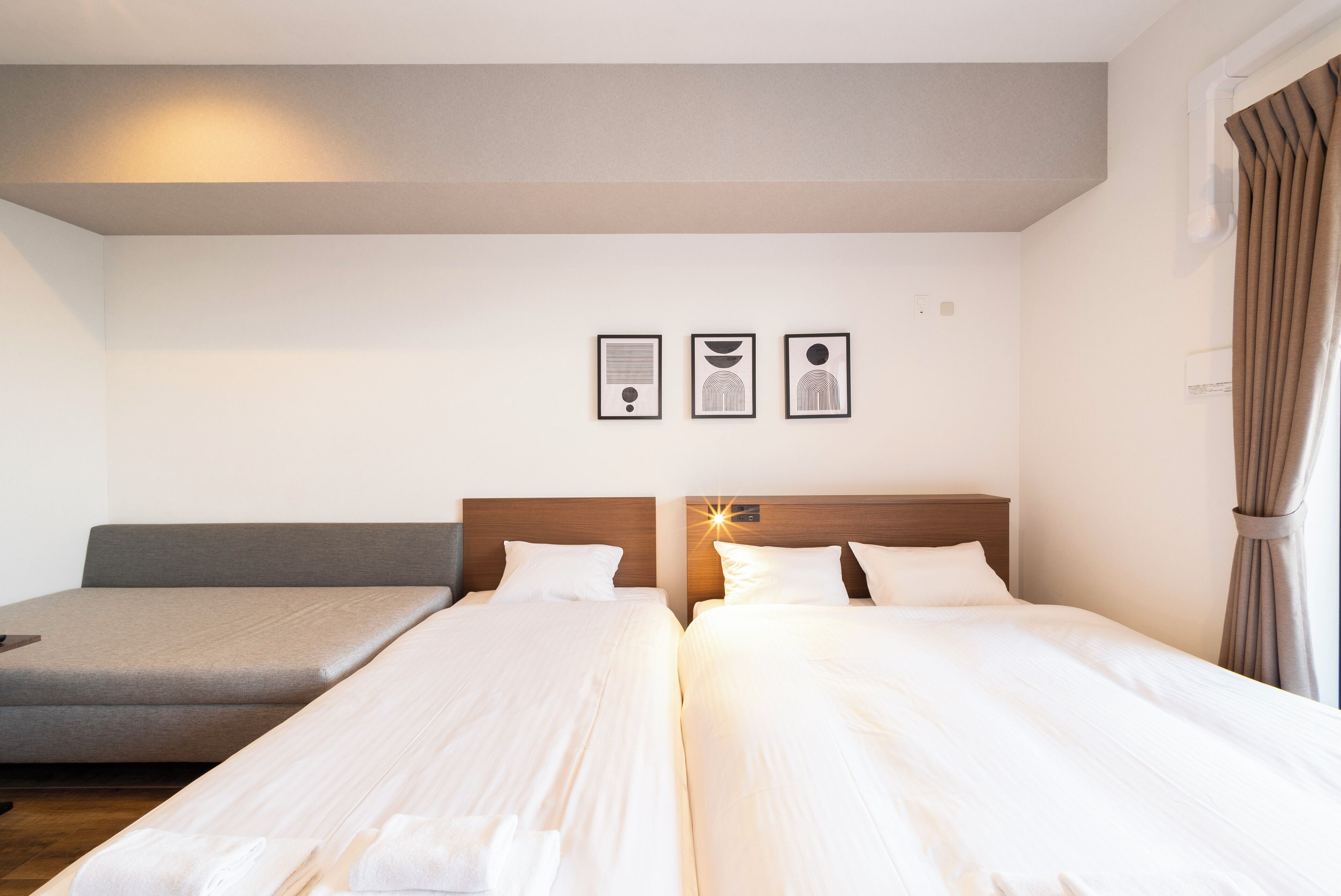 A hotel room with two single beds, a sofa, and three framed pictures on the wall.