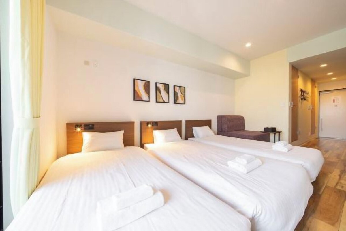 A hotel room with three beds, a wooden headboard, and a small seating area.