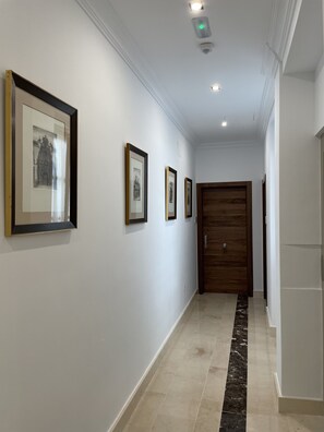 Un pasillo con cuadros enmarcados en la pared, una puerta de madera y un piso de mármol.