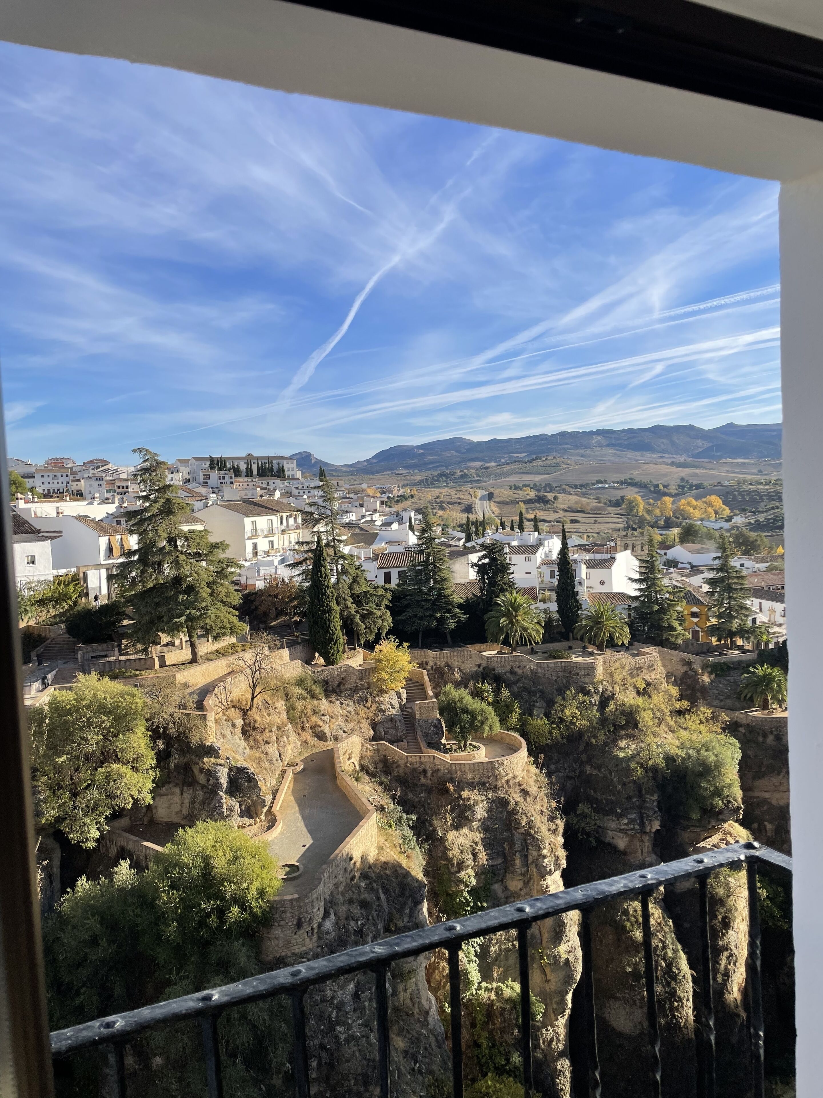 A view from a balcony overlooking a town with historic buildings, a clear sky, and a rocky landscape.