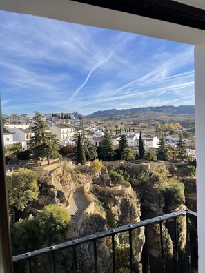 Vista desde un balcón sobre un pueblo con edificios históricos, cielo despejado y paisaje rocoso.