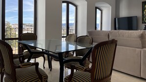 A modern living room with a glass dining table surrounded by striped chairs, a beige sofa, and a flat-screen TV on the wall. - Casa-Palacio Santa Pola (Ronda)