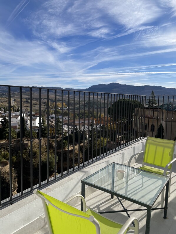 Un balcon doté de balustrades en verre, deux chaises vertes et une table en verre.