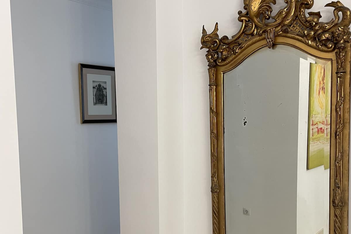 A hallway with a large ornate mirror, a framed picture on the wall, and a tiled floor.