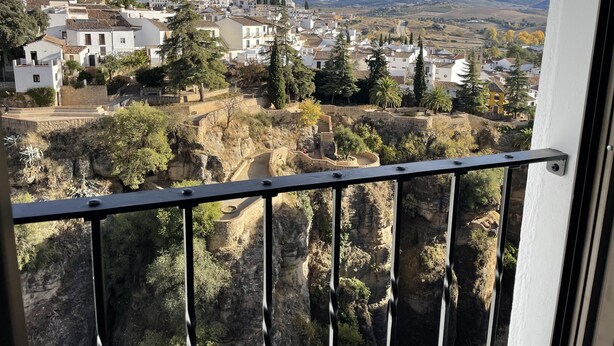 A balcony with a view of a hillside town, stone walls, and a clear sky. - Casa-Palacio Santa Pola (Ronda)