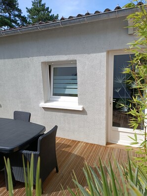 Een terras met een tafel en stoelen, een klein raam en een deur die leidt naar een buitenruimte.