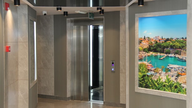 An elevator interior with a digital display, marble walls, and a framed scenic view of a harbor. - Zenia Otel (Antalya)