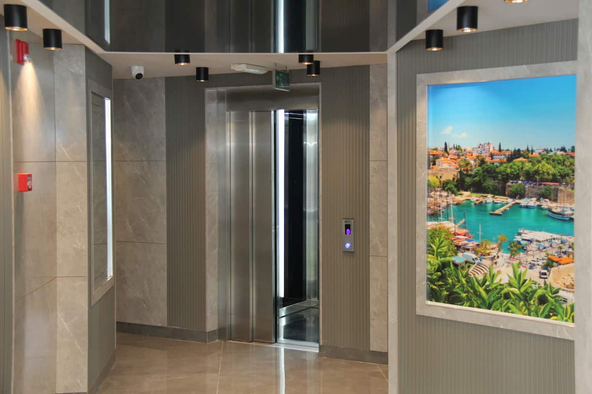 An elevator interior with a digital display, marble walls, and a framed scenic view of a harbor.