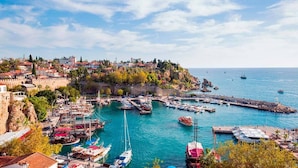 A coastal town with a marina filled with boats, a historic fort, and buildings on a hillside. - Zenia Otel (Antalya)