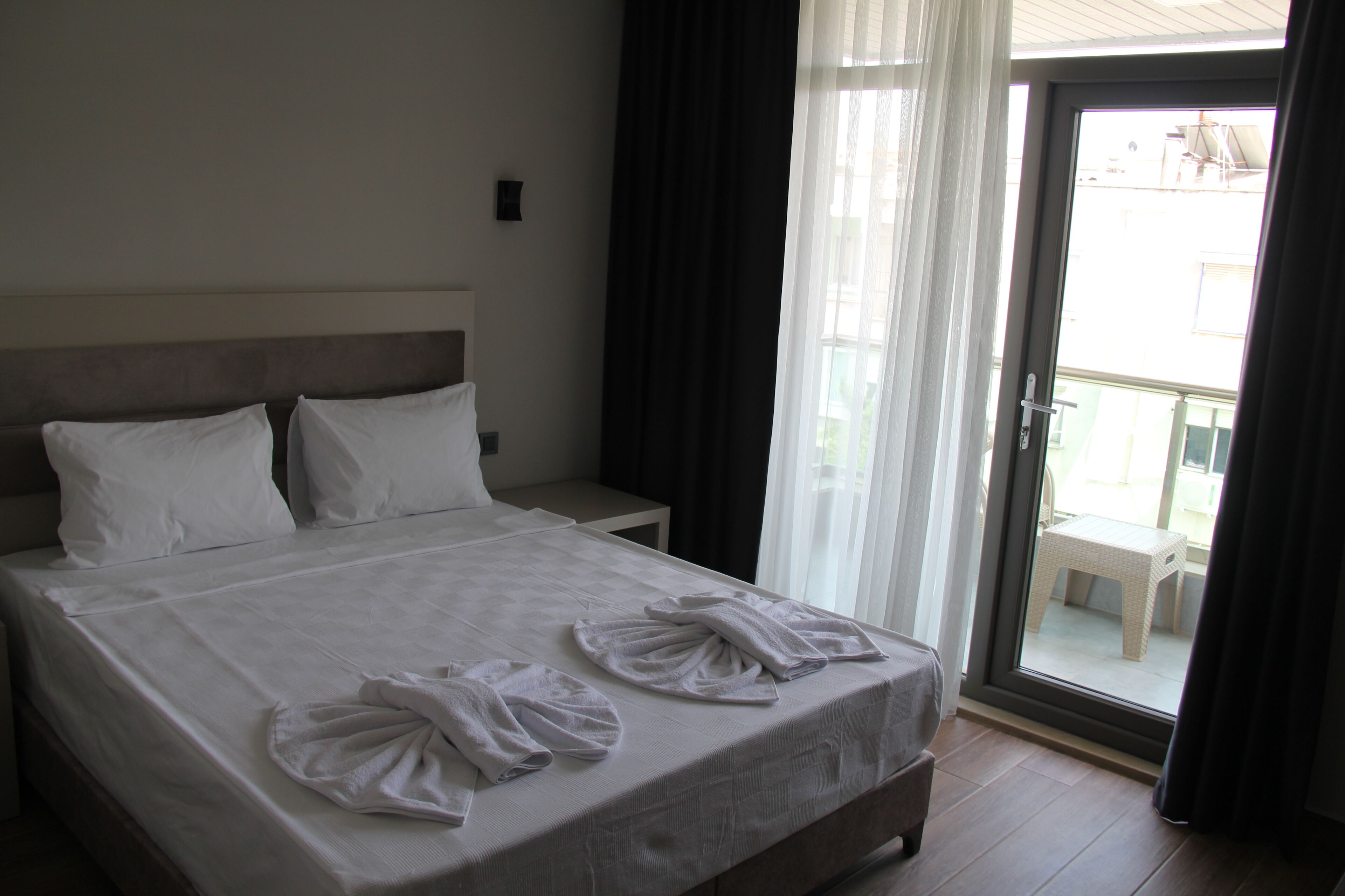 A hotel room with a bed, a nightstand, a window with curtains, and a view of the outside.