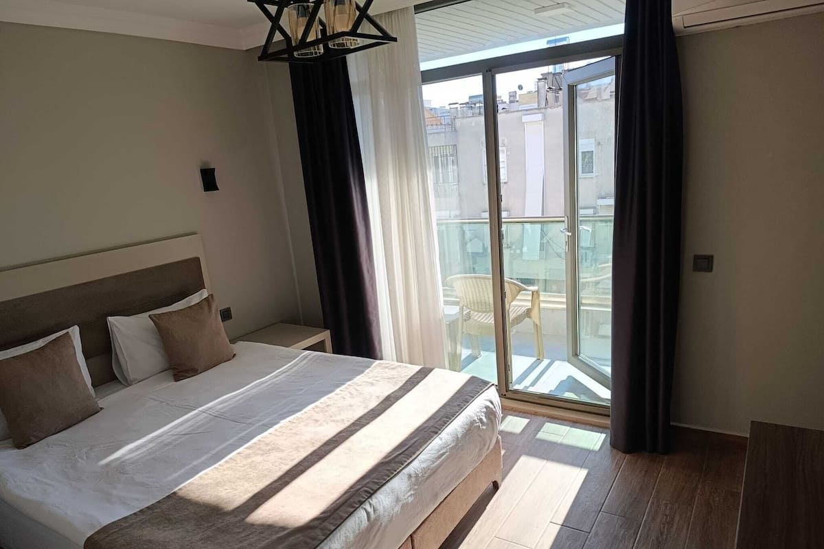 A hotel room with a large bed, a balcony with a chair, and a view of buildings.
