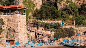 A stone building with a terrace and a pool area with sun loungers and umbrellas. - Zenia Otel (Antalya)