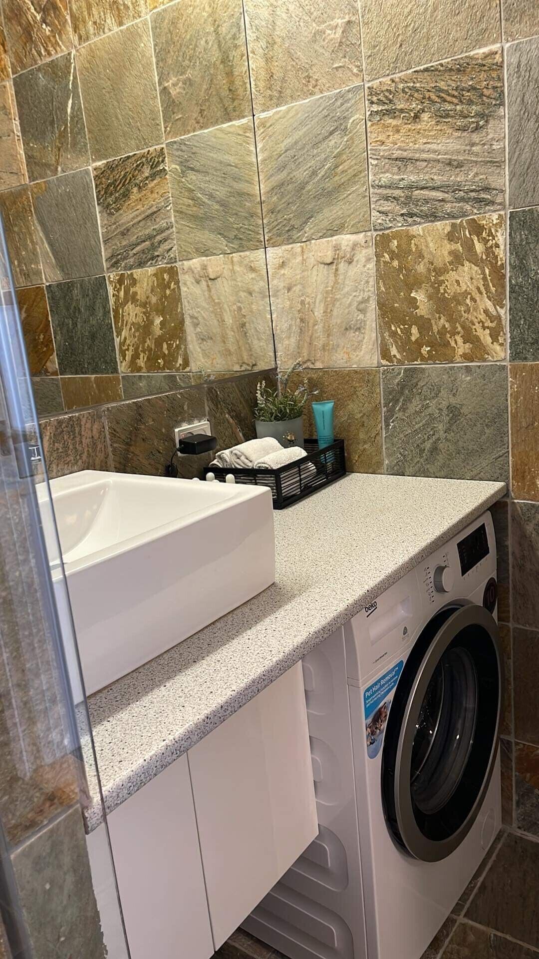 A compact bathroom with a white sink, a washing machine, and a tiled wall.