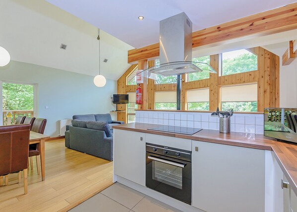 A modern kitchen with wooden beams, a built-in oven, and a dining area with a sofa and table.