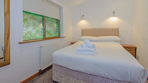 A bedroom with a bed, a window with a view, a radiator, and two bedside lamps. - A superbly appointed impressive two storey luxury lodge. (Llangollen)