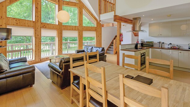 A spacious living area with a wooden dining table, a sofa, and a kitchen area with cabinets and a stove. - A superbly appointed impressive two storey luxury lodge. (Llangollen)