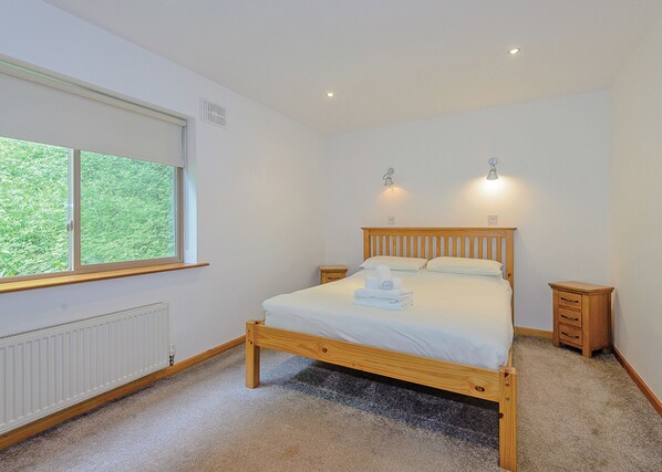 A bedroom with a wooden bed, a window, a radiator, and two bedside tables. - A superbly appointed impressive two storey luxury lodge. (Llangollen)
