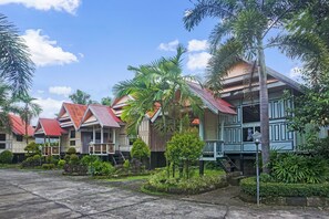 A row of traditional wooden houses with red roofs, surrounded by lush greenery and palm trees. - OYO 90923 Makassar Cottage (Makassar)