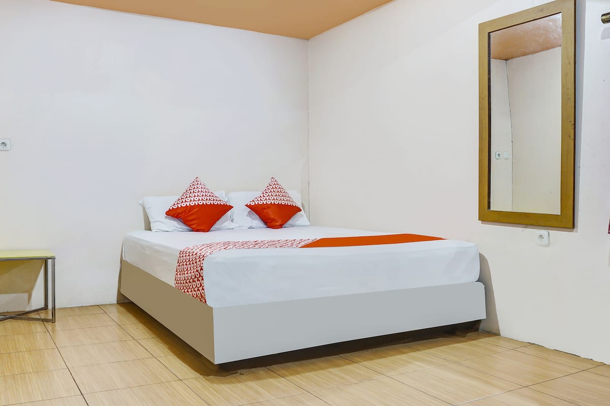 Ein Schlafzimmer mit einem Bett, Kissen, einem Nachttisch und einem Spiegel an der Wand.