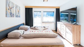 A bedroom with a bed, a TV, a window with curtains, and artwork on the wall. - Apartment with Terrace (Oetz)