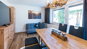 A modern kitchen with wooden cabinets, a blue sofa, a dining table with candles, and a large window with a view of greenery. - Apartment with Terrace (Oetz)