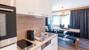 A modern kitchen with a built-in oven, a coffee machine, and a dishwasher. There is a dining area with a wooden table and chairs. - Apartment with Terrace (Oetz)