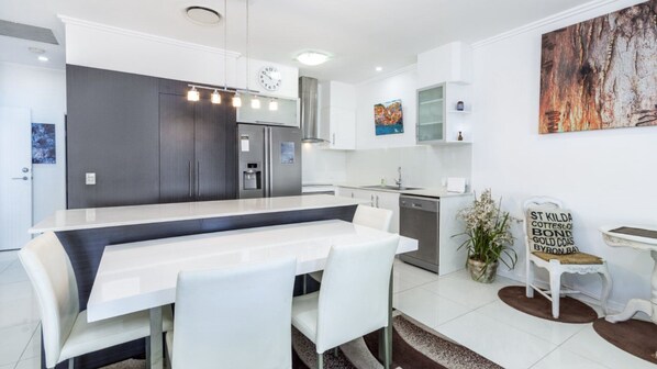 A modern kitchen with a central island, white cabinetry, and a dining area with a white table and chairs.