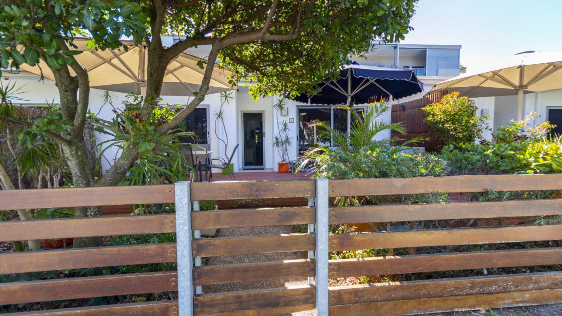 A wooden bench in front of a building with a covered outdoor area, potted plants, and a clear sky.
