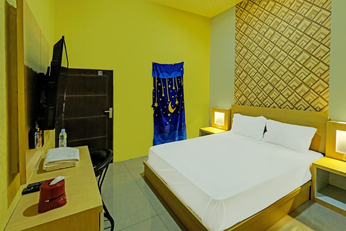 Habitación de hotel con cama, mesitas de noche, escritorio con lámpara, una silla y cortina con diseño de estrella y luna.